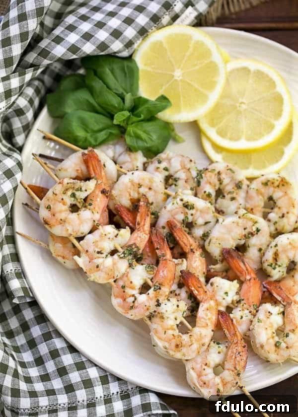 Grilled Shrimp Scampi - A phenomenal shrimp dish cooked on the BBQ Grilled Shrimp Scampi on skewers on a serving plate with basil and lemon slices.