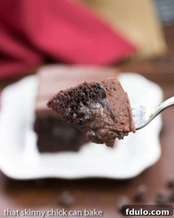 Triple Chocolate Poke Cake - A super moist chocolate cake with fudgy filling and chocolate buttercream! A fork taking a bite out of a Triple Chocolate Poke Cake, revealing the fudgy filling inside the moist chocolate cake.