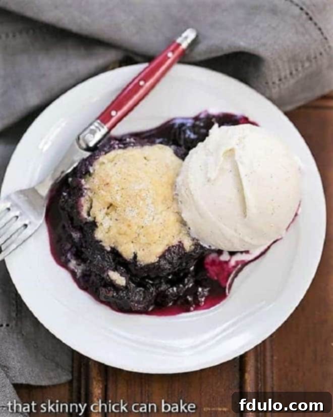 A serving of Grilled Blueberry Cobbler a la mode on a white plate with a red handled fork, highlighting its rustic appeal and delicious topping.