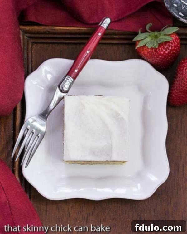 Overhead view of a slice of white sheet cake on a white plate with a red handled fork, emphasizing its delightful frosting.