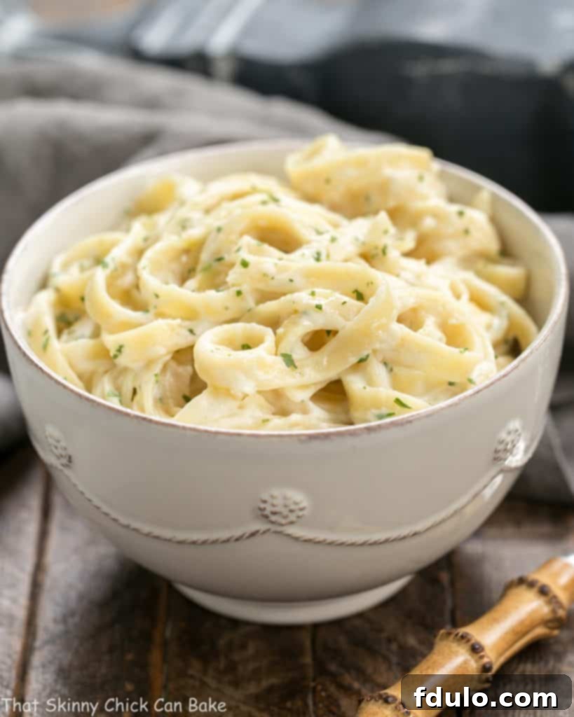 Light Fettuccine Alfredo in a white bowl garnished with fresh parsley, emphasizing its creamy texture.