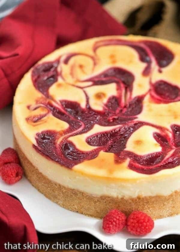 A slice of White Chocolate Raspberry Swirl Cheesecake on a white plate garnished with fresh raspberries, showcasing the vibrant swirls and creamy texture.