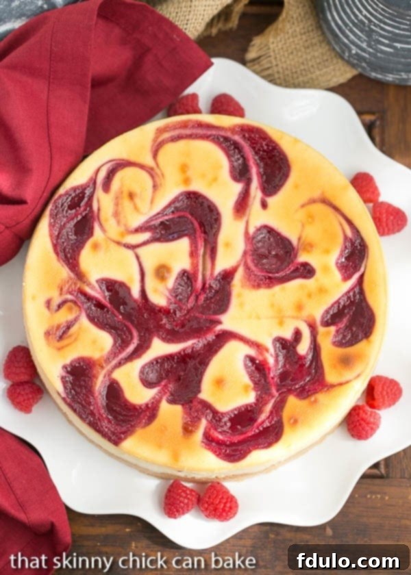 Overhead view of White Chocolate Raspberry Swirl Cheesecake on a white serving plate with fresh raspberries, showcasing the beautiful swirl.