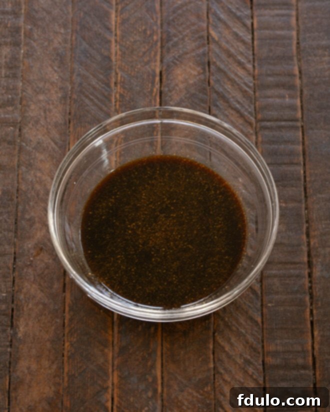 A bowl containing the salmon marinade ingredients: maple syrup, soy sauce, minced garlic, and ground ginger, ready to be mixed.