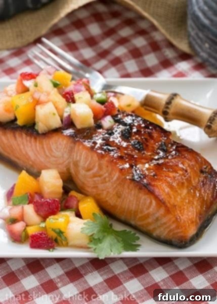A perfectly broiled Maple Glazed Salmon fillet on a white plate, beautifully topped with a colorful and refreshing fruit salsa, ready to be served.