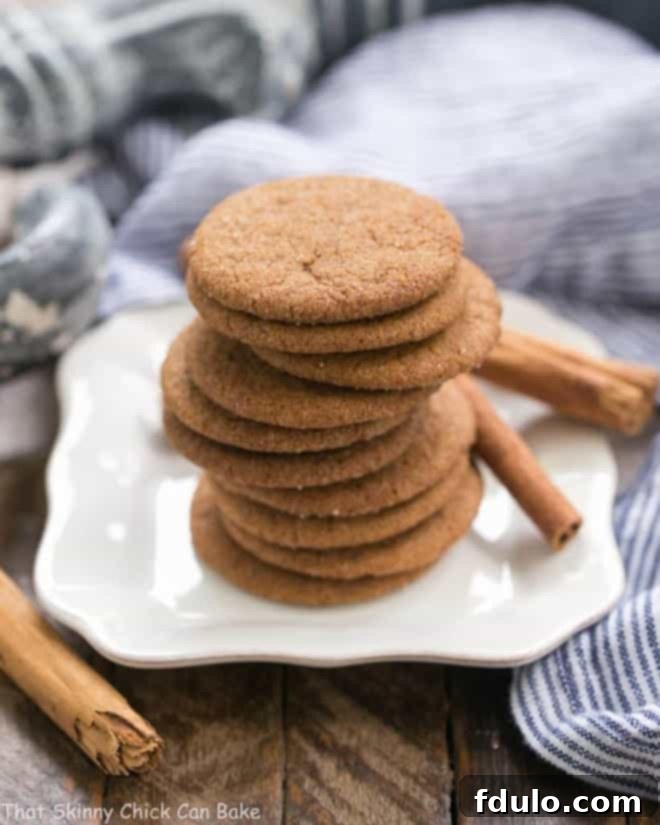 Holiday Ginger Crisps stacked neatly on a white plate, adorned with cinnamon sticks and a festive backdrop, hinting at a cozy holiday season