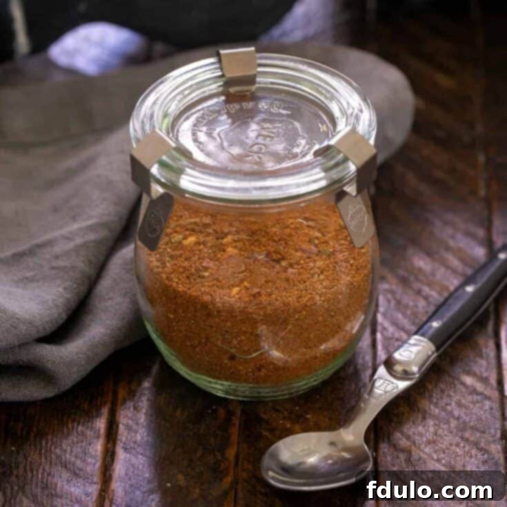 Square image of Taco seasoning in a glass container with a black handled spoon, highlighting its homemade quality.