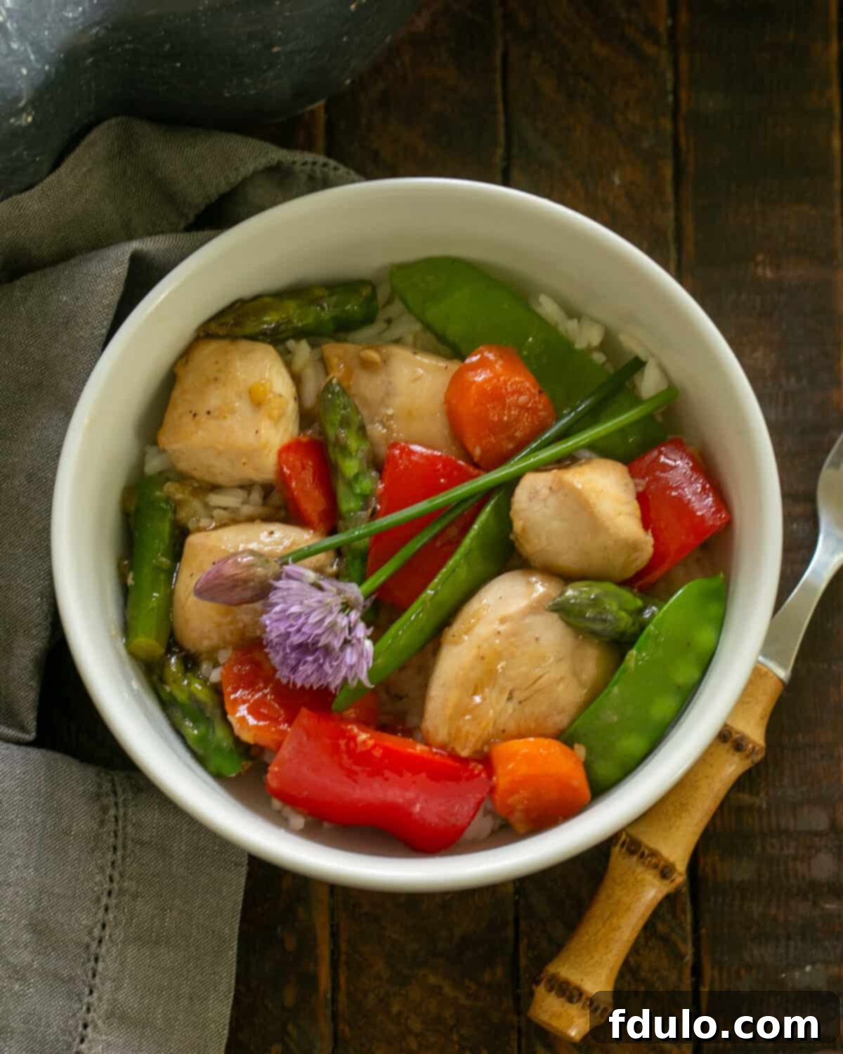 Close-up of Chicken Stir Fry in a white bowl, garnished with fresh chives and a fork, highlighting its freshness.