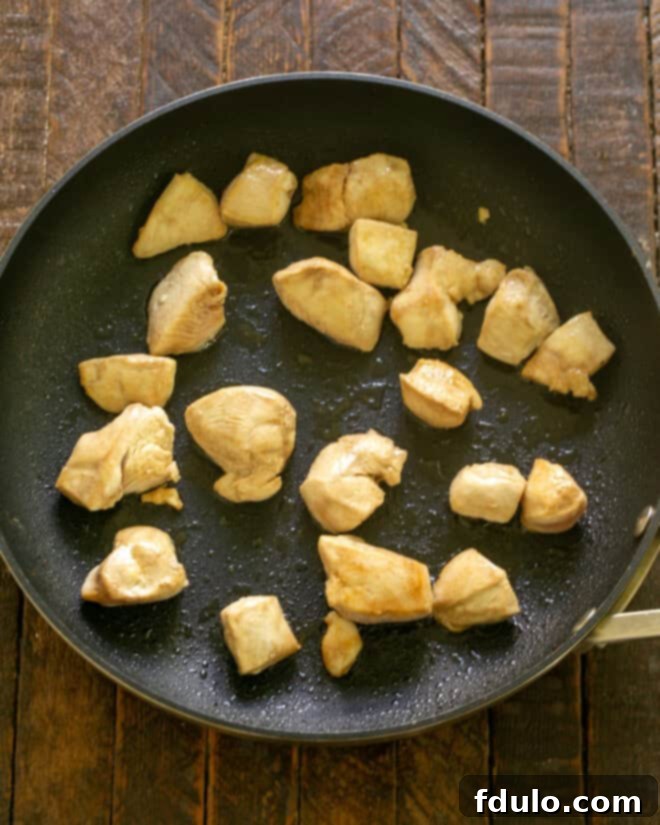 Chicken cooking in a hot wok, browning in batches.