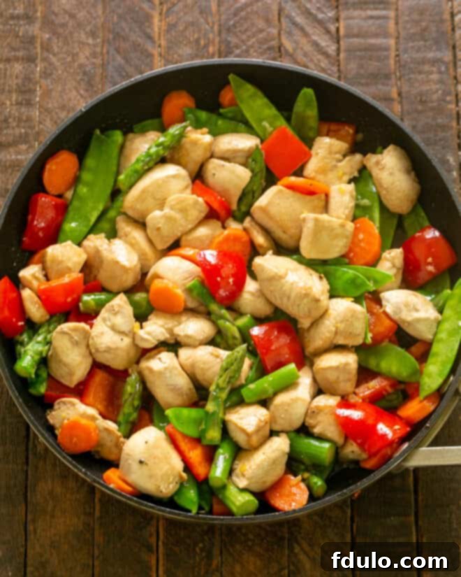Cooked chicken being returned to the wok with stir-fried vegetables.
