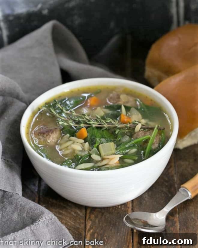 A close-up shot of Italian wedding soup in a white bowl, garnished with fresh herbs and served with a bamboo-handled spoon, showcasing the rich broth, meatballs, and greens.