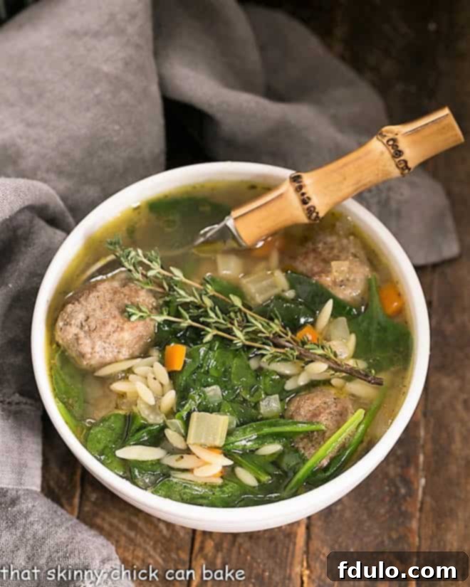 Overhead view of a steaming bowl of Italian Wedding Soup with a bamboo-handled spoon, showing a meatball, spinach, and pasta ready to be enjoyed.