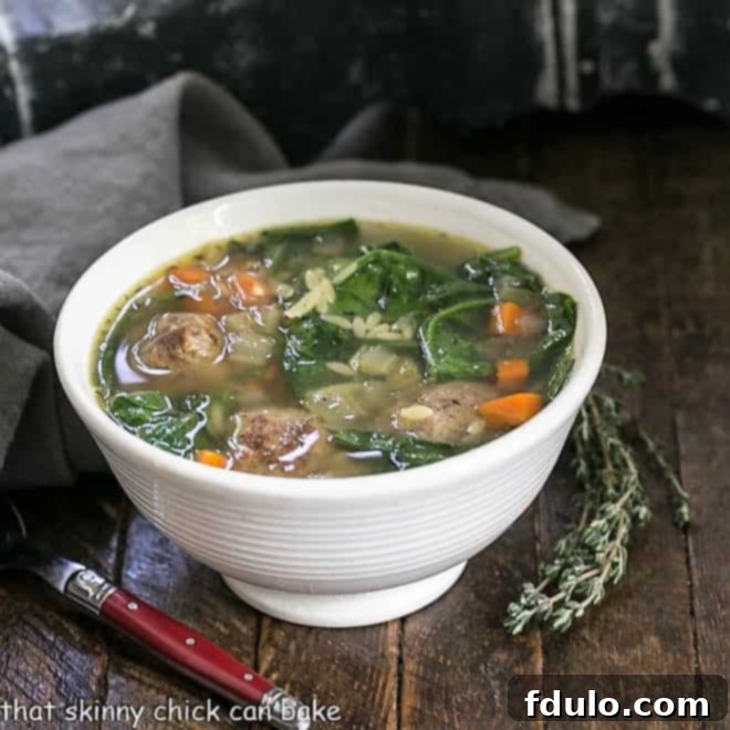 Italian wedding soup in a white bowl with a sprig of thyme
