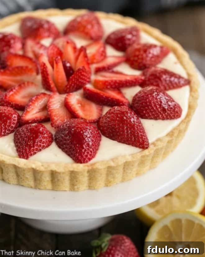 A luscious, easy to make Strawberry Lemon Tart made with lemon curd and topped with sweet, sliced berries A beautifully presented Strawberry Lemon Tart on a pristine white cake stand, showcasing vibrant red strawberries atop a pale yellow lemon curd filling.