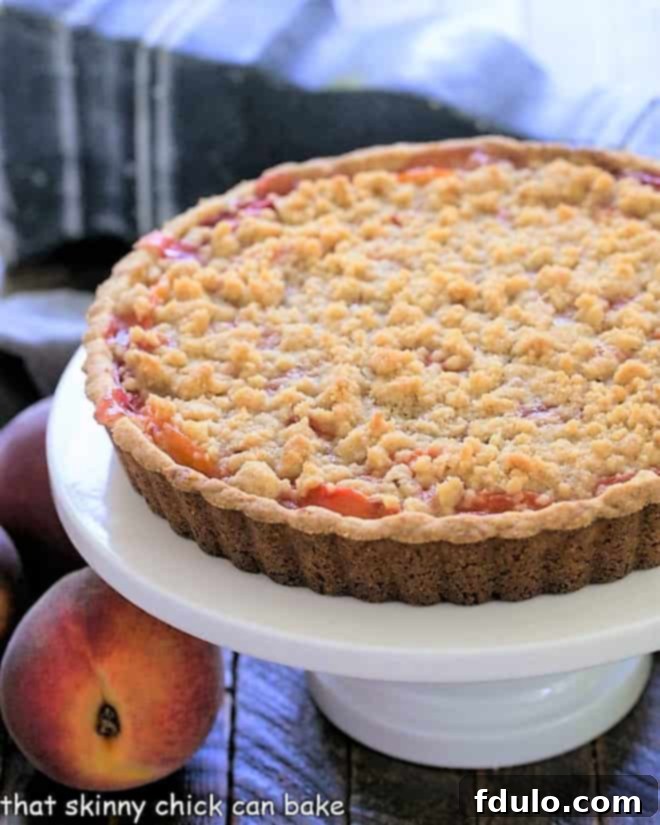 Streusel Topped Peach Tart on a white ceramic cake stand, showcasing its golden crumb topping and juicy peach filling.