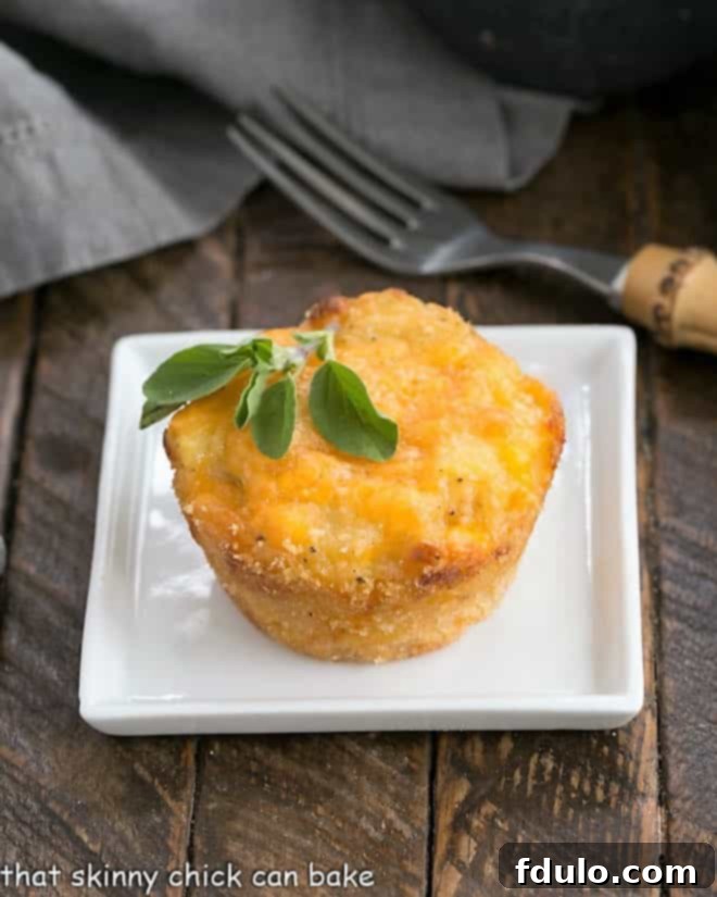 Individual Cheesy Potato Bake - a delicious cheese potato recipe the whole family will love A single golden-brown Cheesy Potato Cup on a square white plate, garnished with a sprig of fresh herbs.