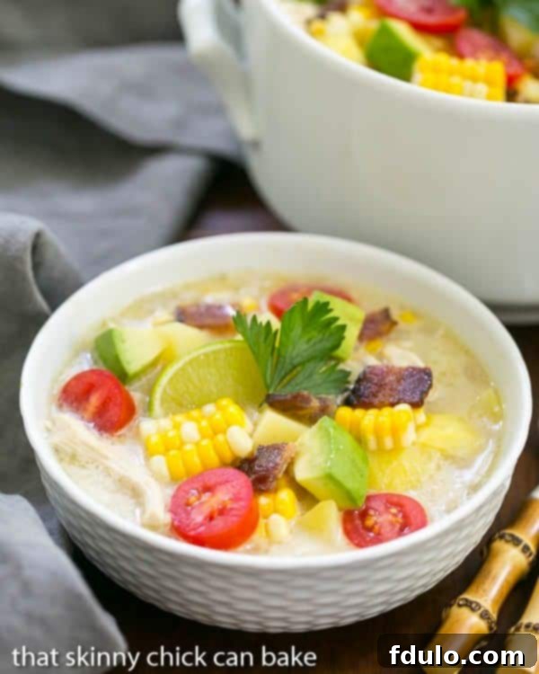 Bacon Corn Chowder - A summer soup full of corn, potatoes, chicken and smoky bacon! A white bowl filled with corn chowder with a large pot behind it.