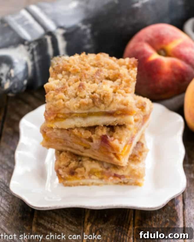 3 Fresh peach bars stacked on a square white plate, showcasing layers of crust, peaches, and streusel