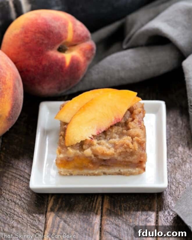 Fresh Peach Pie Bar on a white plate topped with peach slices, highlighting the golden streusel