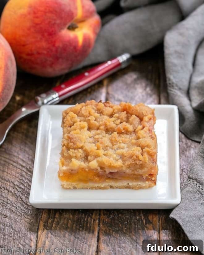A single fresh peach bar on a square white plate, showcasing its golden-brown crust and juicy peach filling