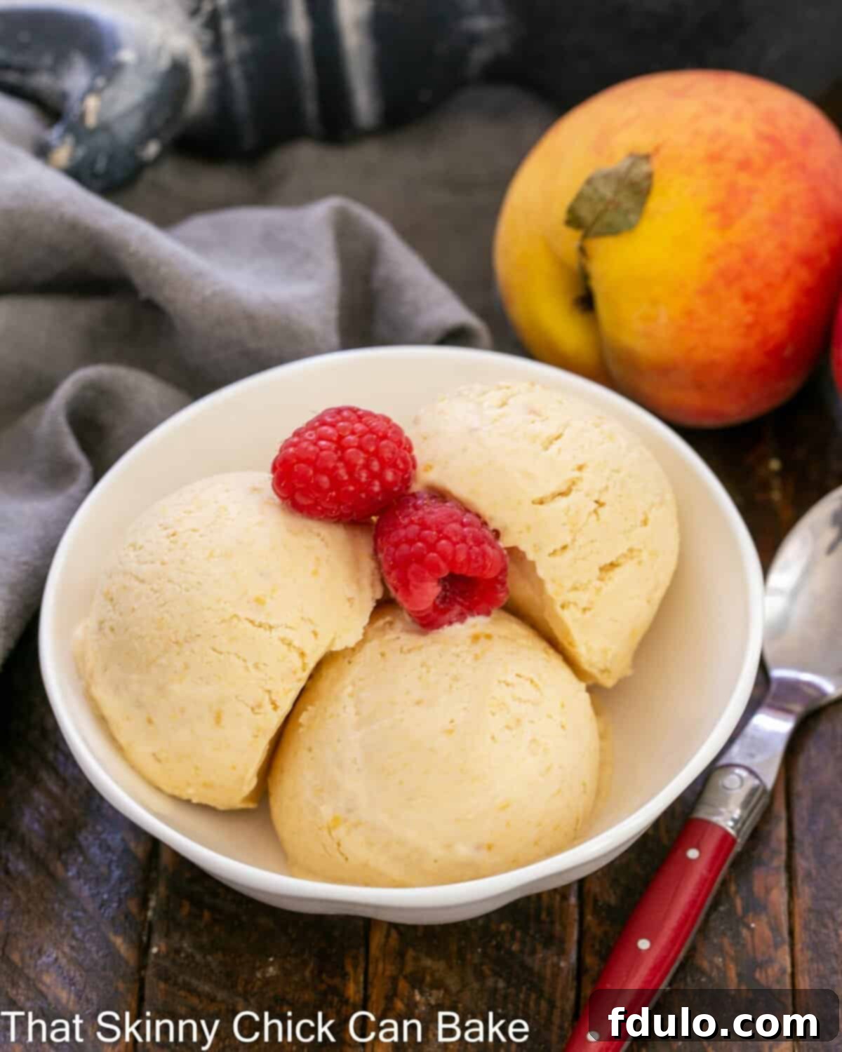 No- Churn Peach ice cream in a shallow bowl with raspberry garnish.