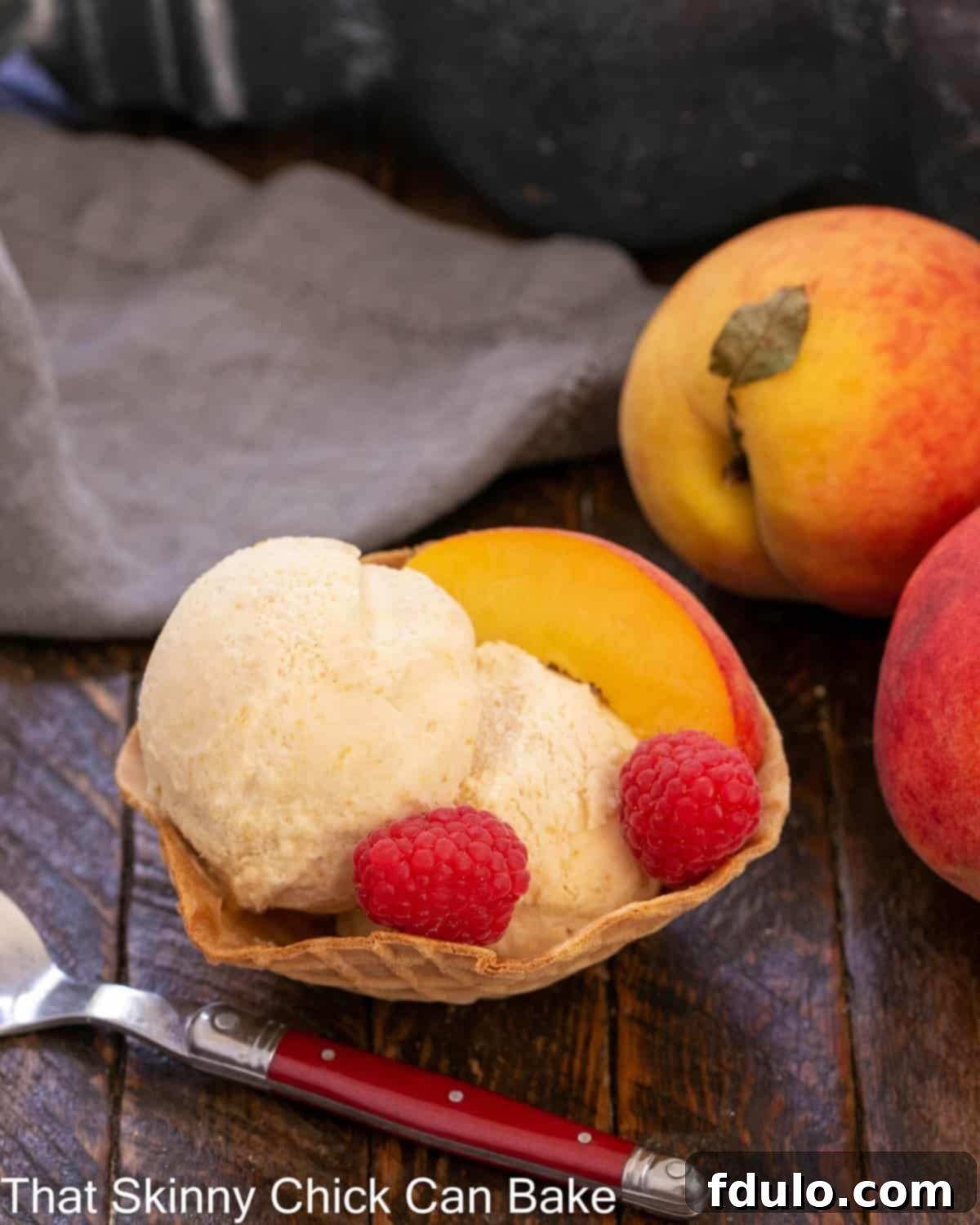 No-churn peach ice cream in a sugar cone bowl with raspberry and peach garnishes.