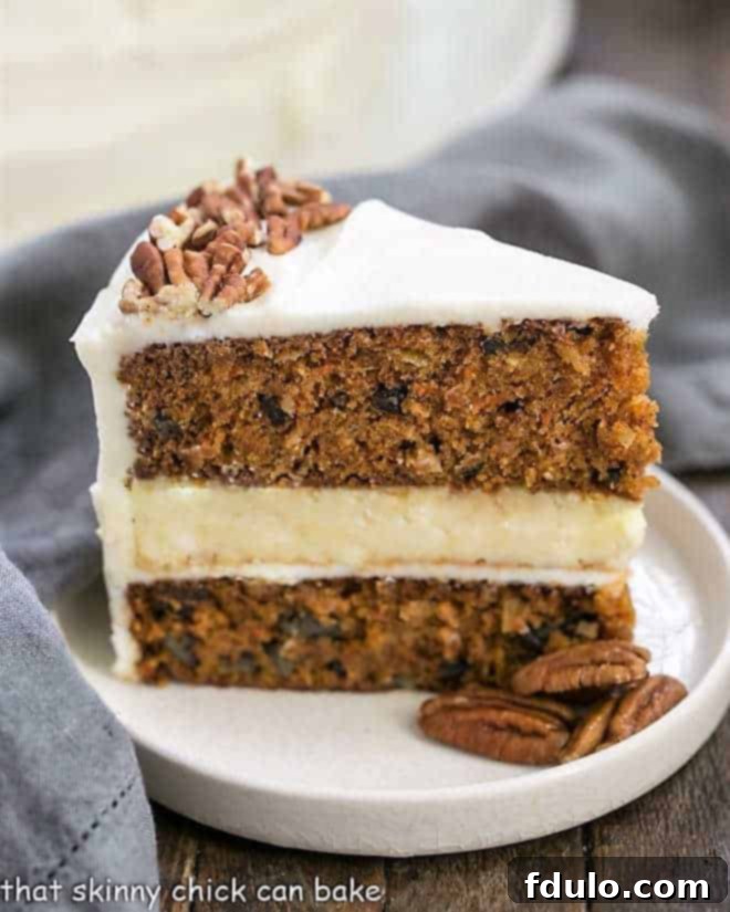 A perfectly cut slice of Cheesecake Filled Carrot Cake on a white rimmed plate, garnished with chopped pecans and a hint of cream cheese frosting. The distinct layers of moist carrot cake and creamy cheesecake are clearly visible.