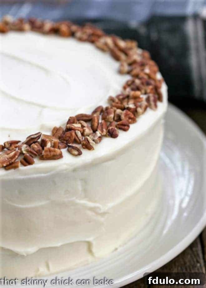 A partial overhead view of a magnificent whole cheesecake stuffed carrot cake, expertly frosted with a rich cream cheese frosting and garnished with a ring of chopped pecans on top.