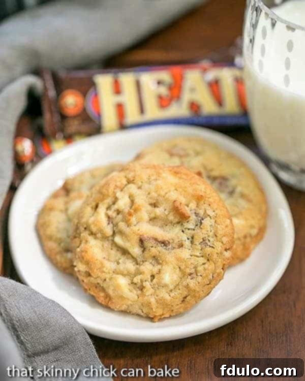 Irresistible White Chocolate Toffee Chunk Cookies on a pristine white ceramic plate, served alongside a refreshing glass of milk, highlighting their golden brown exterior and visible chunks of white chocolate and toffee.