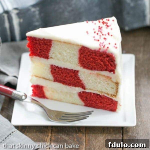 A perfectly sliced piece of Red Velvet Checkerboard Cake on a white dessert plate, showcasing the distinct red and white checkered pattern.
