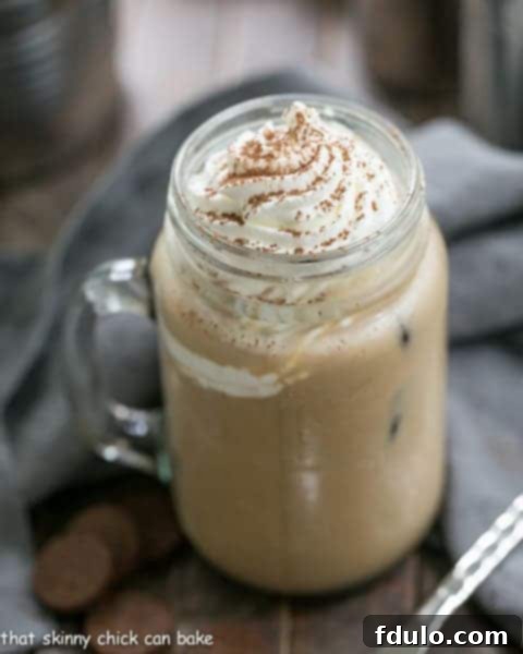 Vanilla Bean Iced Coffee served in a clear glass with a straw, garnished with whipped cream.