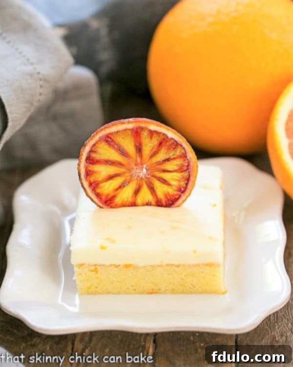 Exquisite Orange Cake with Cream Cheese Frosting on a square white plate, garnished with fresh orange slices and a sprig of mint, showcasing its inviting texture.