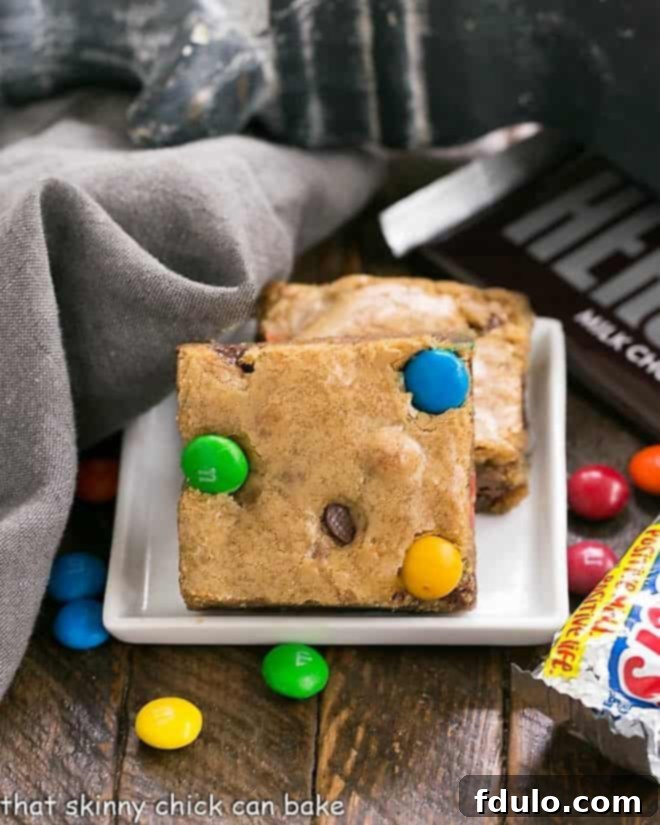 Candy Bar Blondies - The perfect way to use up any leftover candy! Two perfectly cut Candy Bar Blondies, featuring a rich, chewy texture and visible candy pieces, presented on a chic square white plate.