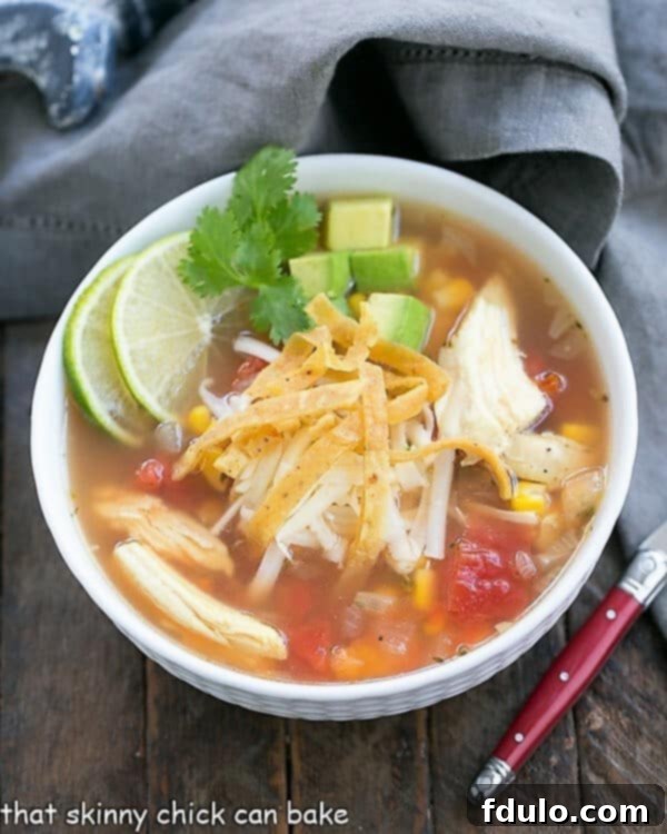 A steaming bowl of Leftover Turkey Tortilla Soup, garnished with fresh cilantro and a lime wedge, served with a red handled spoon.