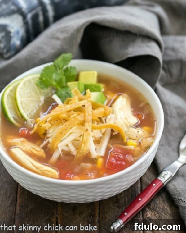 A white bowl of Leftover Turkey Tortilla Soup, garnished with lime wedges and fresh cilantro sprigs.