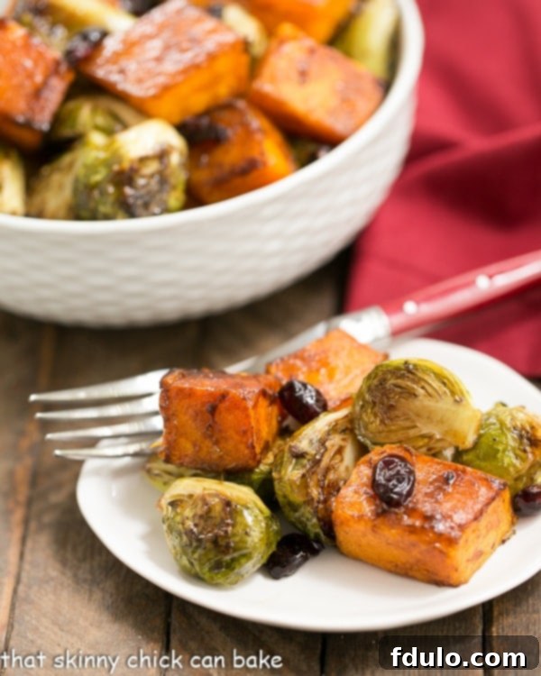 Roasted Autumn Vegetables - Squash, Brussels sprouts and dried cranberry party together for a magnificent side dish! Roasted Autumn Vegetables on a small white plate with a bowl of roasted vegetables in the background.