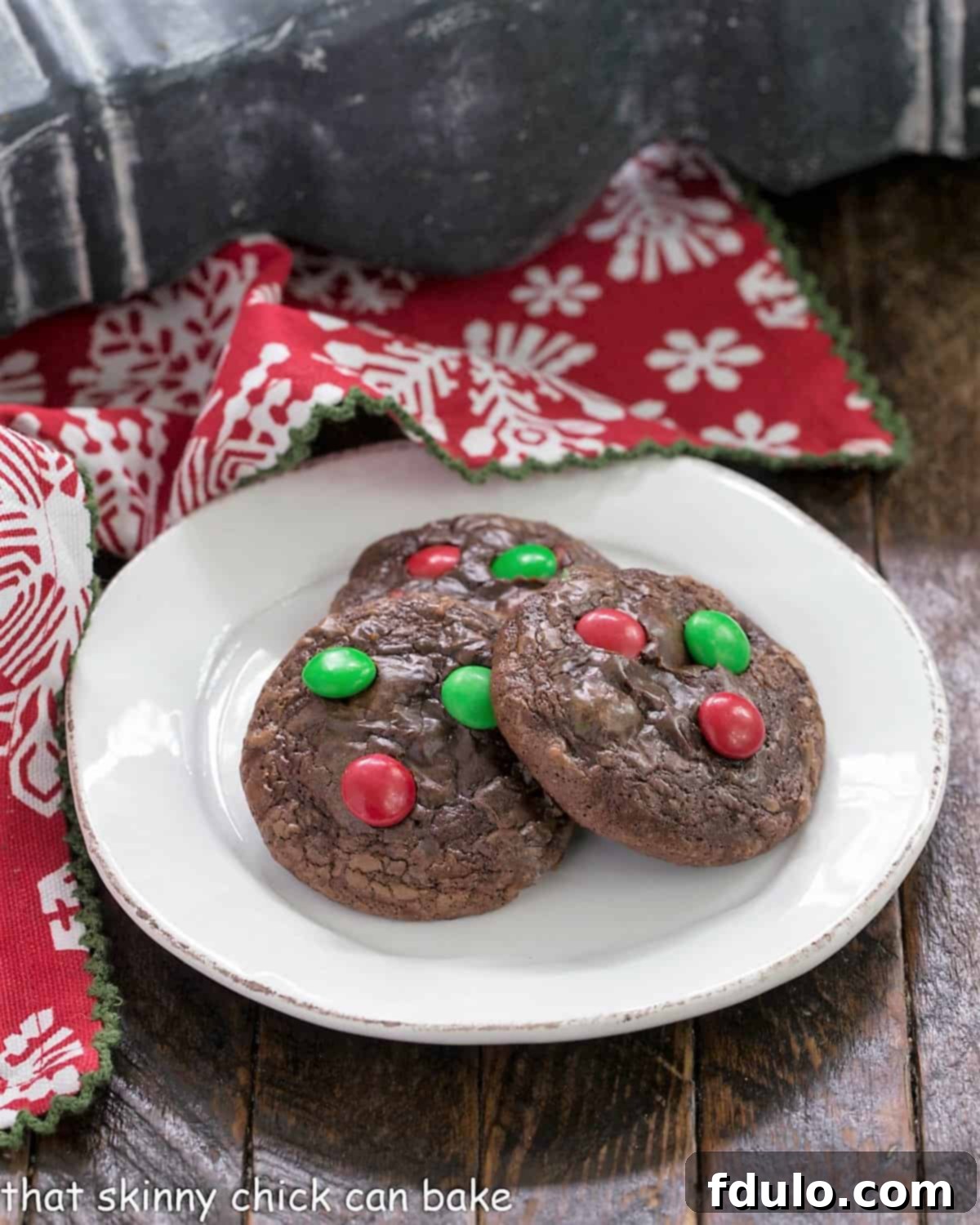 Three decadent Holiday Truffle Cookies, studded with bright red and green M&M's, artfully arranged on a round white plate, evoking a festive and inviting sense of holiday indulgence.