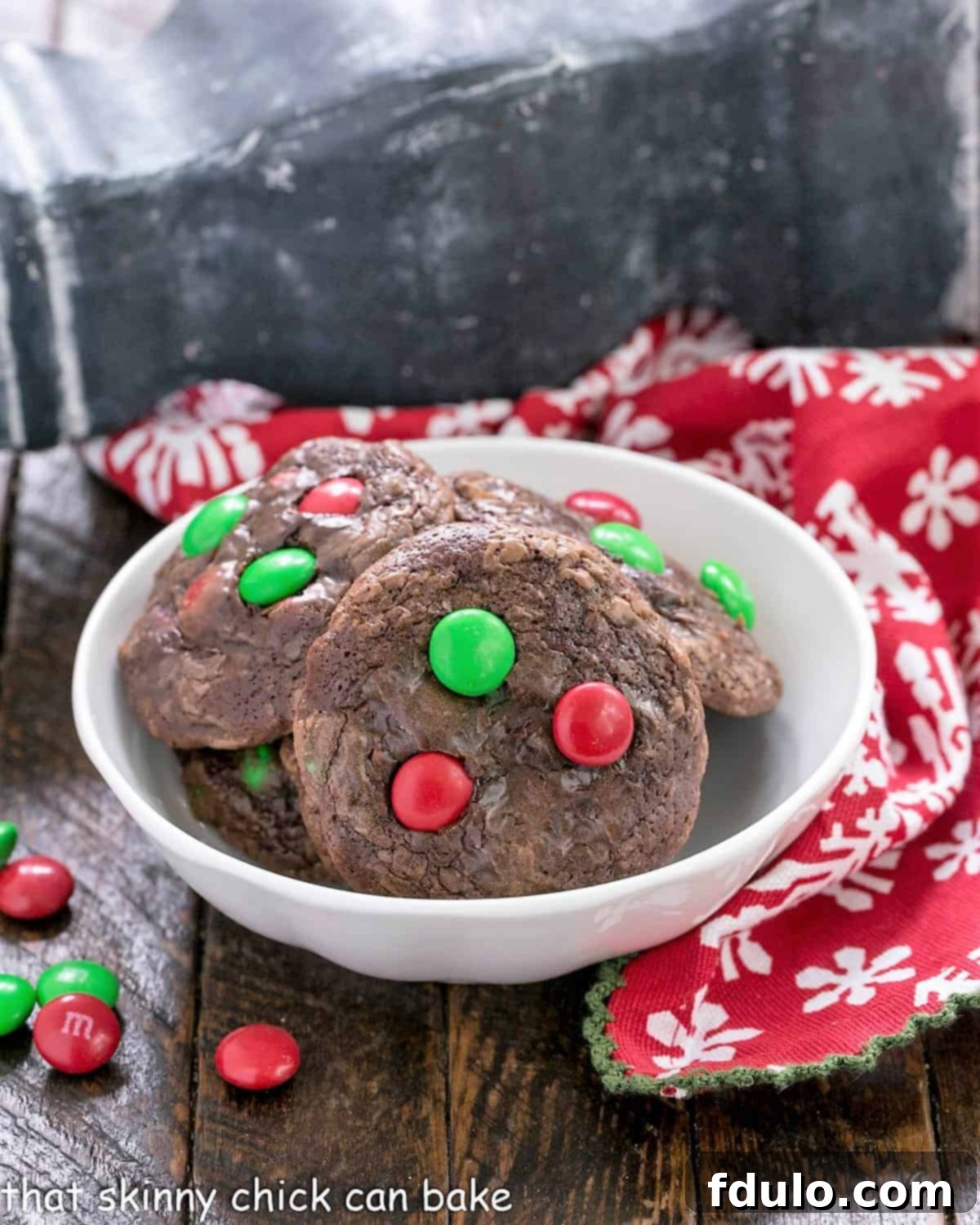 A small white bowl brimming with festive Holiday Truffle Cookies, elegantly surrounded by a scattering of bright red and green M&M's, creating a delightful and inviting holiday scene, perfect for sharing and enjoyment.
