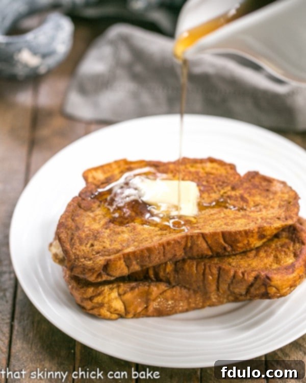 Close-up shot of Pumpkin French Toast, showcasing its golden-brown texture and fluffy interior, generously topped with white mascarpone whipped cream and glistening maple syrup, ready to be enjoyed.