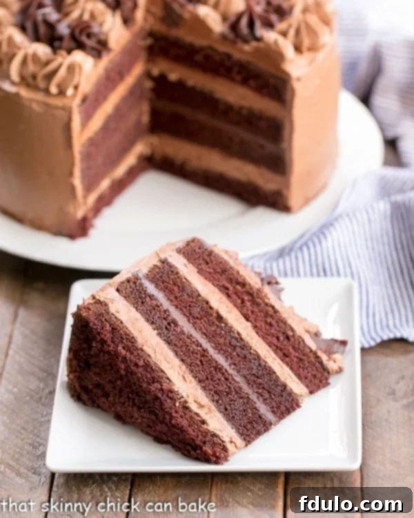 Chocolate Fudge Layer Cake with a slice on a square white plate with cut cake in the background.