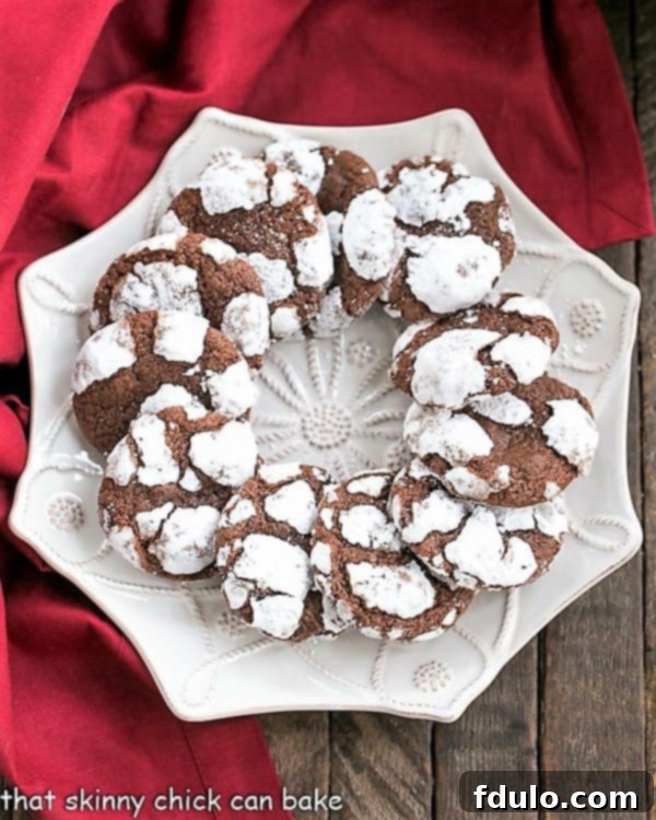 A festive arrangement of Chocolate Crinkle Cookies, showing their distinct cracks and powdered sugar coating, on a white serving plate.