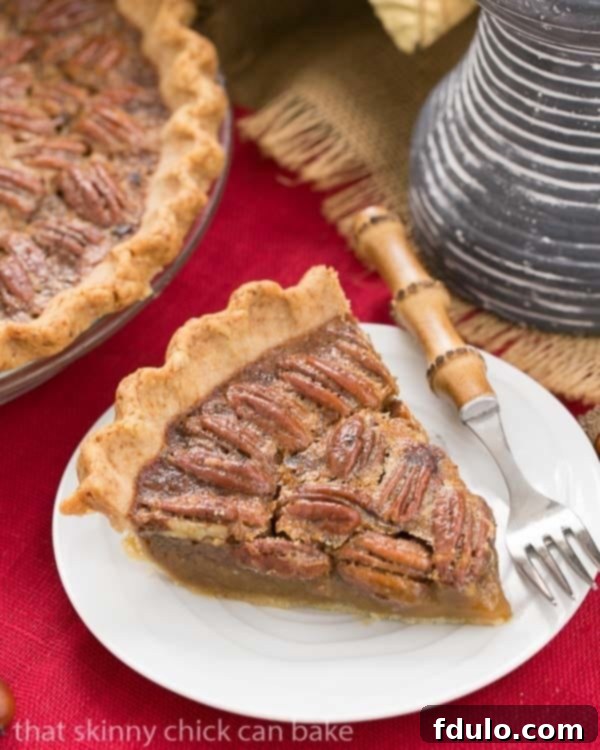 Classic Pecan Pie, with a boozy twist! - A rich, ultra-sweet indulgence. Perfect for the holidays! Classic Pecan Pie, with a boozy twist on a white dessert plate with a bamboo handled fork.