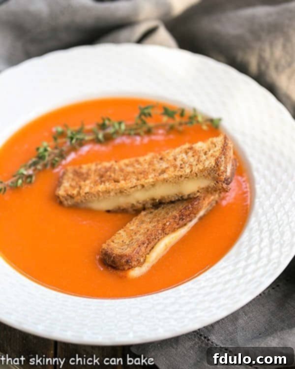 Homemade Tomato Soup with Thyme - A luscious classic made without cream and served with grilled cheese fingers! A steaming bowl of creamy homemade tomato soup with fresh thyme, garnished with small grilled cheese triangles.