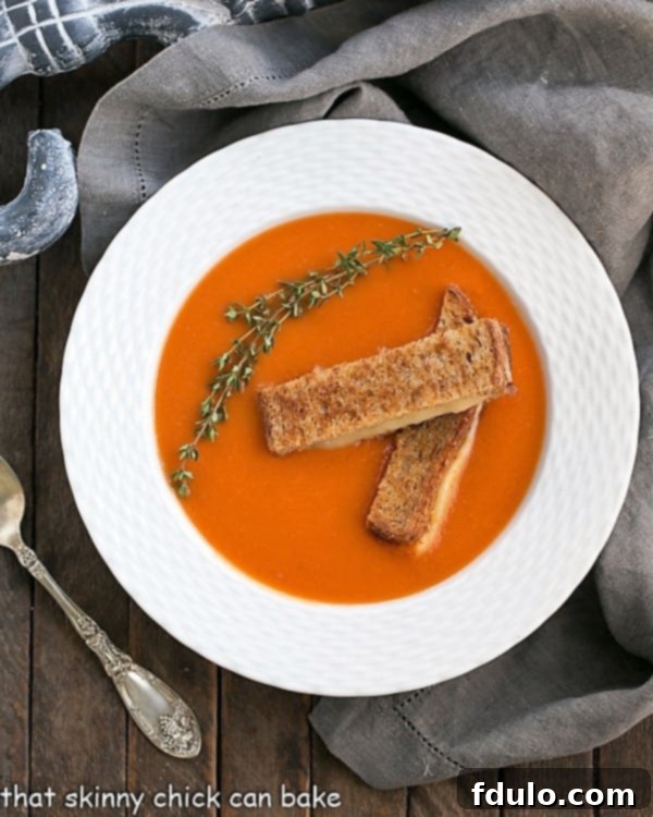 Homemade Tomato Soup - A luscious classic made without cream and served with grilled cheese fingers! An overhead view of a white bowl filled with creamy homemade tomato soup, garnished with a sprig of thyme.