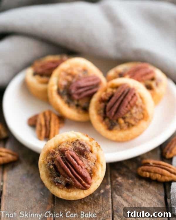 Pecan Tassies - Irresistible Mini Pecan Pies with a luscious cream cheese pastry crust. Rich, flavorful, and perfectly portioned! Delightful Pecan Tassies adorned with golden pecan halves, elegantly presented on a pristine white plate, ready for a bite-sized dessert.