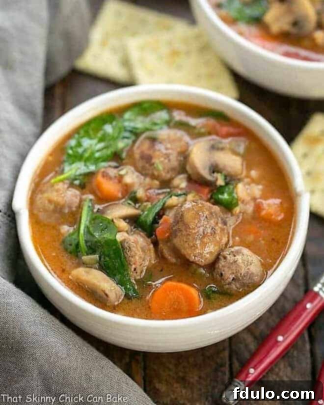 A steaming bowl of Rustic Farro Soup, brimming with vegetables, Italian sausage, and chewy farro, with a red-handled spoon resting inside, ready to be enjoyed.