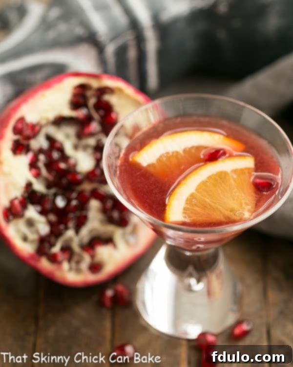 Overhead view of a Pomegranate Champagne Cocktail in a flute, with half a pomegranate and loose arils on the side, set against a dark background.
