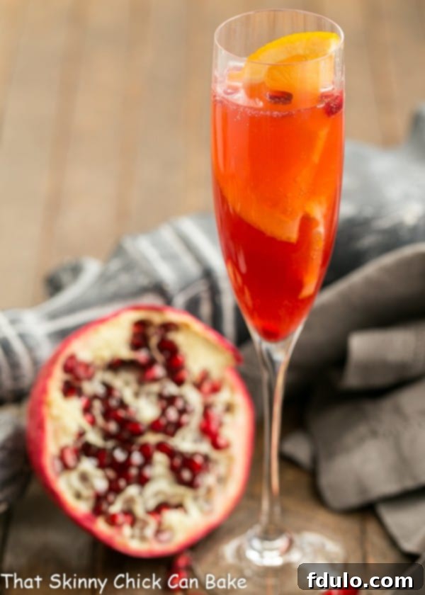 Pomegranate Champagne Cocktail in a champagne flute with a half pomegranate and fresh lime slices