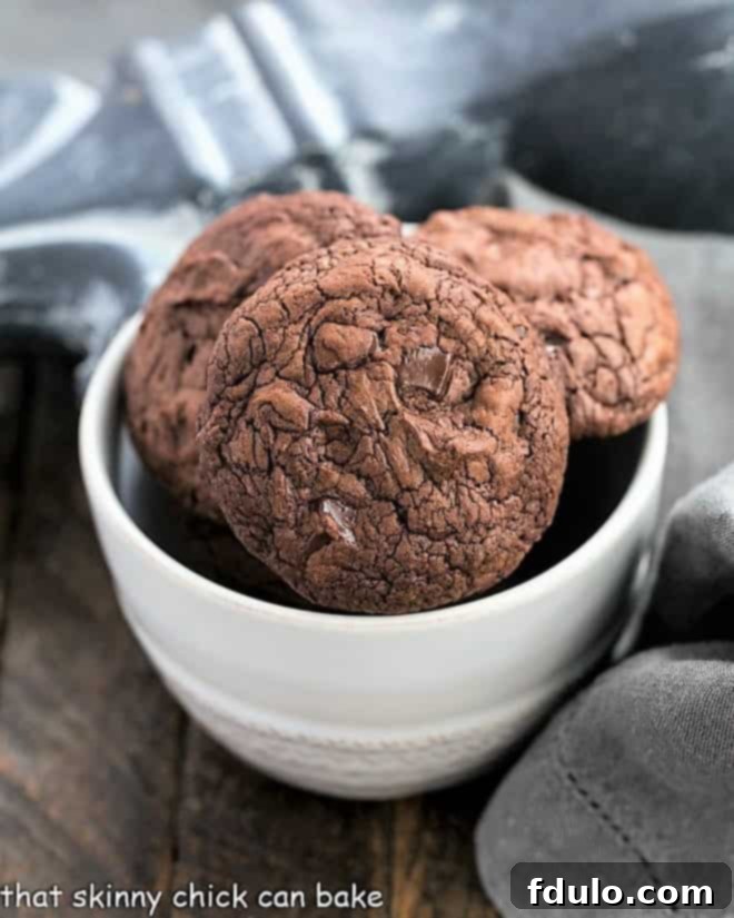 Black Gold Cookies - a chocoholic's dream featuring two types of chocolate, generous chunks, and minimal flour for ultimate fudginess! Black Gold Cookies in a small white bowl, showcasing their rich, dark color and inviting texture.