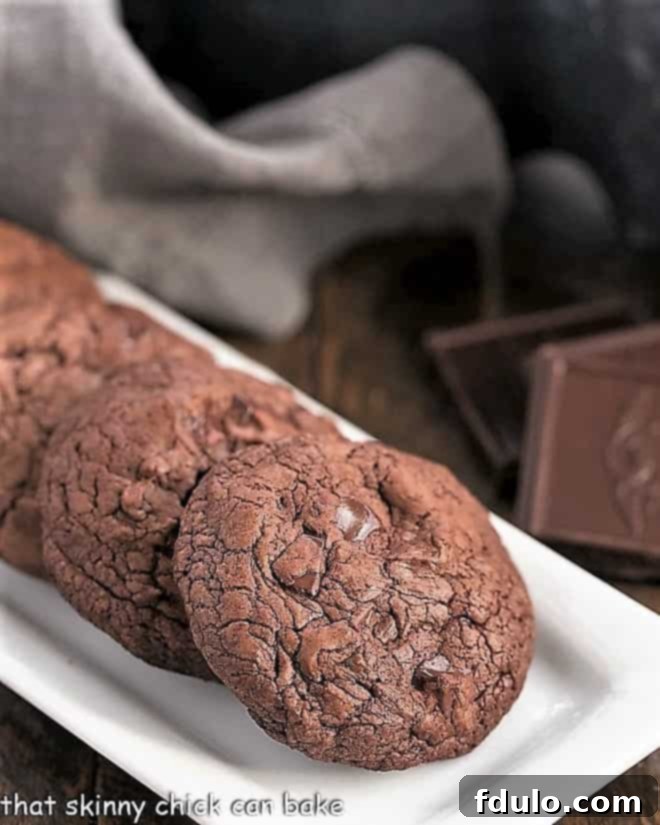 Black Gold Cookies - a chocoholic's dream featuring two types of chocolate, generous chunks and minimal flour, ensuring ultimate fudginess! Black Gold Cookies perfectly lined up on a pristine white rectangular tray, emphasizing their uniformity and delicious appeal.